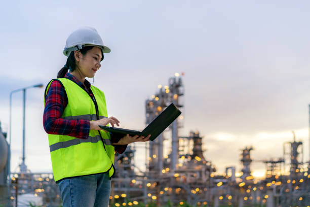 Asian woman petrochemical engineer working at night with notebook Inside oil and gas refinery plant industry factory at night for inspector safety quality control.