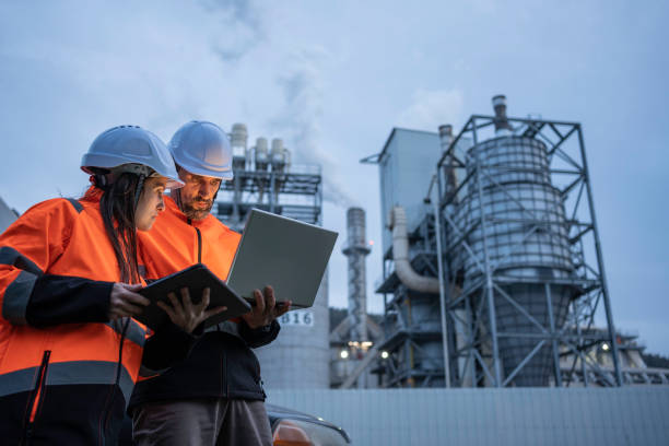 Man and woman working late with laptop in a power plant. Night shift.