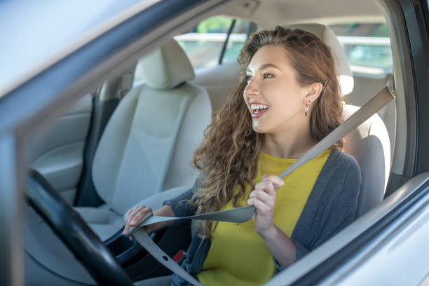 Seat belt. Smiling joyful young woman holding a safety belt while driving while sitting in a car